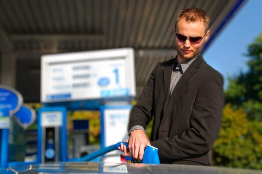 Young man in a dark suit standing at the gas station and filled up his silver sports car