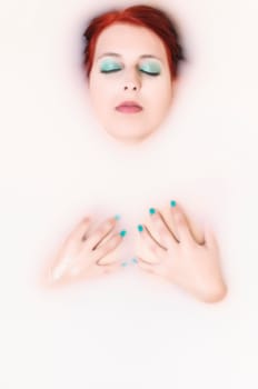 Beauty woman in bathroom with water with milk covering her breasts with her hands.