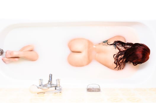Beauty woman with red hair in bathroom with water with milk showing her back und butts.