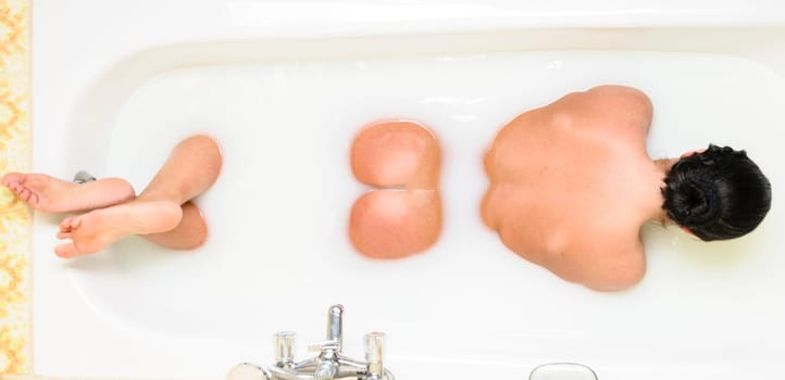Adult woman lying in the bath showing her backsite.
