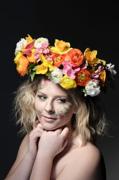 Spring portrait of a young woman with spring-like make-up and a colorful flower wreath in her hair.