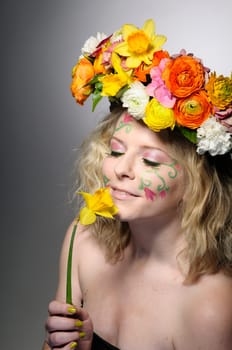 Spring portrait of a young woman with spring-like make-up and a colorful flower wreath in her hair.