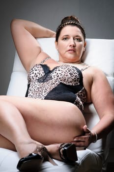 Attractive plus size model wearing lingerie and a bun, lying an a white armchair.