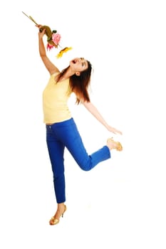 A very tall young Chinese woman dancing for white background in blue dress pants and yellow top, with flowers in her hand.