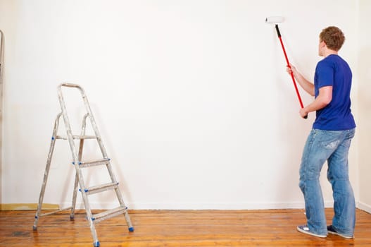 Young man in a T-shirt paints the walls of his first apartment in bright colors.