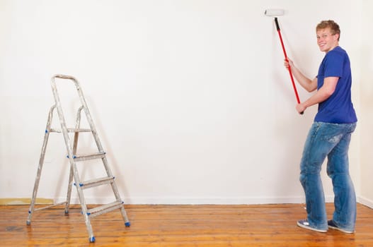 Young man in a T-shirt paints the walls of his first apartment in bright colors.