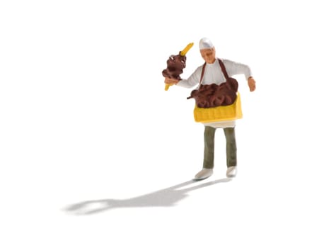 Miniature pretzel seller in white bakers cap and uniform with tray of crispy traditional German pastries around his neck and others displayed on a handheld stick over a white background