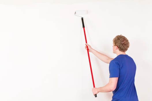 Young man in a T-shirt paints the walls of his first apartment in bright colors.