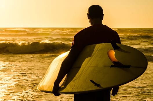 A surfer watching the waves at sunset in Portugal.