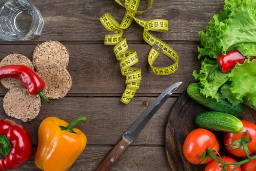 Glass of water with vegetables and measuring tape on wooden table close-up. Copy space. Top view