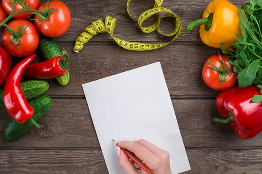 Concept diet, slimming plan with vegetables top view mock up. A female hand in a sports bracelet writes an article about proper nutrition