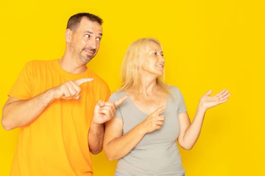 Beautiful caucasian couple in their 40s dressed in casual clothes smiling and looking at the camera pointing with two hands and fingers to the side.