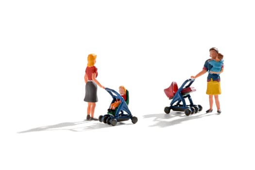 Two miniature figures of young mothers pushing their infants in a pram and pushchair with one holding her baby in her arms as they stand chatting on white