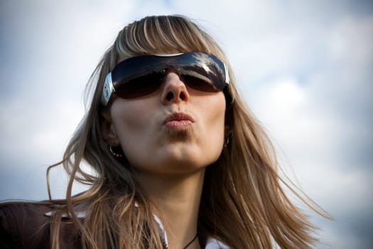 girl in sunglasses with blue sky in background giving a kiss with her lips