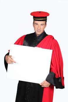 Man in red and black robe and cap pointing at board blank for text