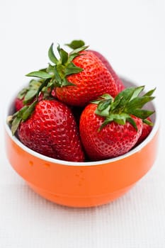 Closeup of large fresh strawberries in orange bowl against light background