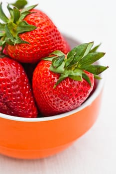 Closeup of large fresh strawberries in orange bowl against light background