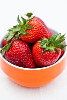 Closeup of large fresh strawberries in orange bowl against light background