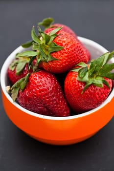 Closeup of large fresh strawberries in orange bowl against dark background