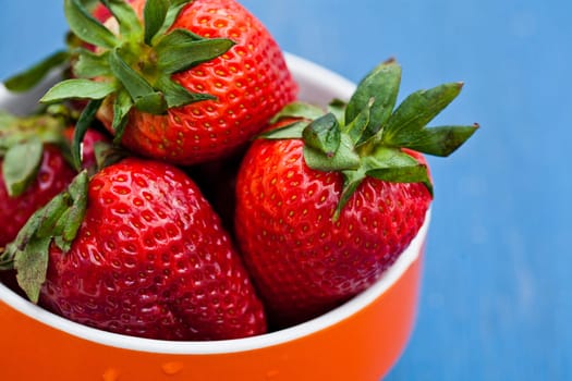Closeup of large fresh strawberries in orange bowl against light blue background