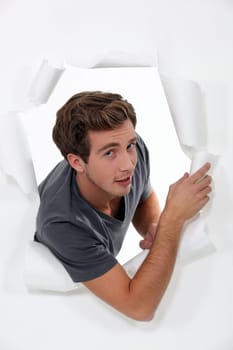 young man looking through hole in torn paper
