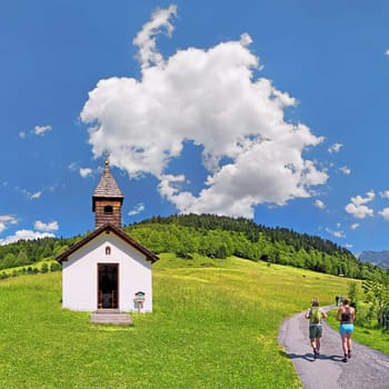 Small chapel at the Graseck with hikers and white-blue sky,Graseck,Garmisch-Partenkirchen,Bavaria,Germany,Europe