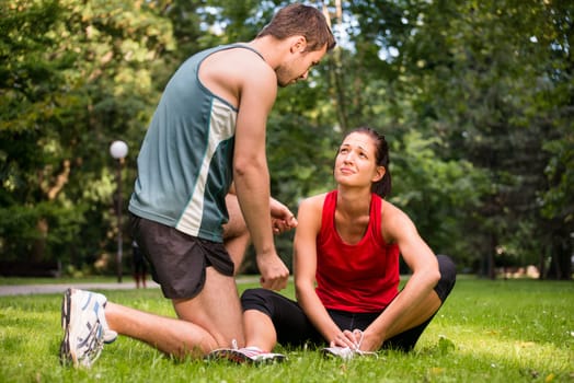 Sport injury - young fitness woman holding her ankle with pain, man is helping