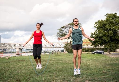 Young fitness couple exercising outdoor - jumping with skipping rope