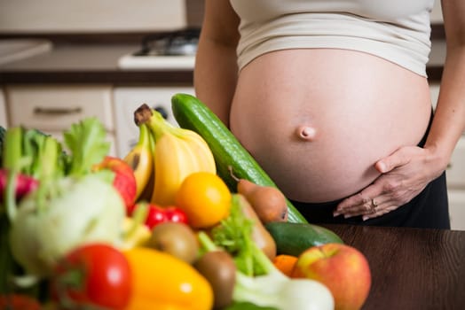 Detail of pregnant woman (belly) with abundance of vegetables and fruits
