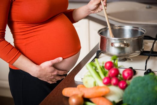 Crop of belly - pregnant woman cooking vegetables in kitchen