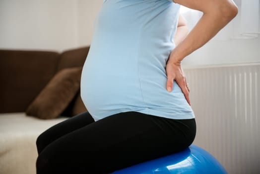 Torso of pregnant woman sitting on fit ball with backache