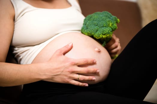 Detail of hands holding pregnant belly and broccoli - indoors