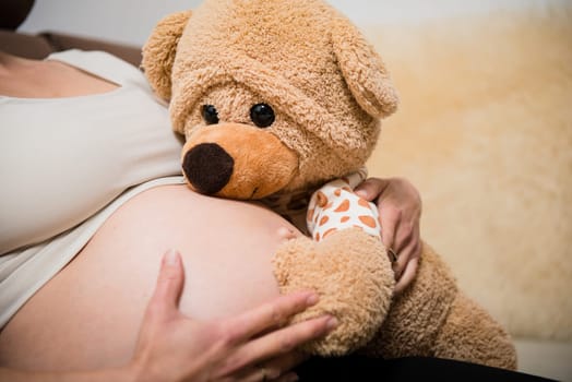 Detail of hands holding pregnant belly - with teddy bear