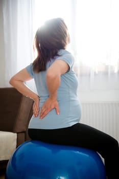 Pregnant woman sitting on fit ball with backache at home