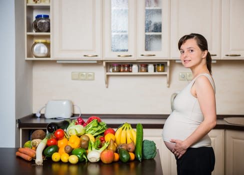 Pregnant woman with abundance of vegetables and fruits in kitchen