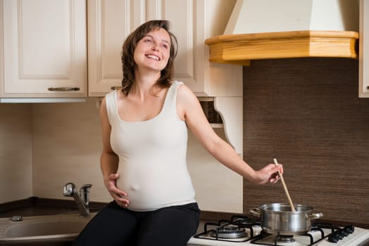 Lifestyle portrait of smiling pregnant woman cooking in home kitchen