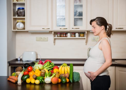 Pregnant woman with abundance of vegetables and fruits in kitchen