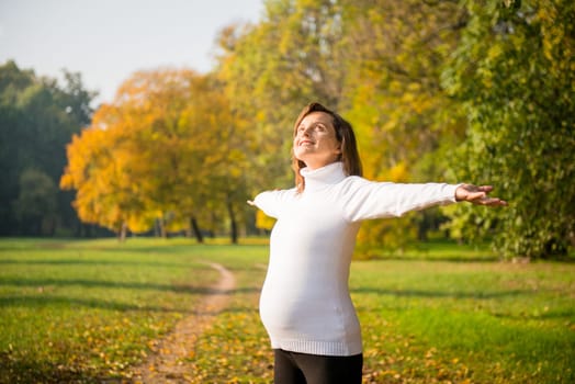 Happy pregnant woman enjoying life outdoors in autumn colorful nature