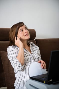 Pregnant woman working on laptop from home and calling phone