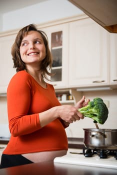 Lifestyle portrait of smiling pregnant woman cooking broccoli in kitchen