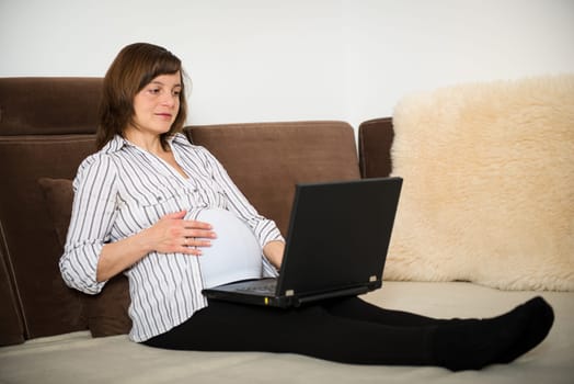 Pregnant woman working on laptop from home on sofa