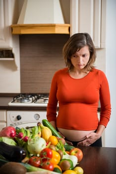 Unhappy pregnant woman with abundance of vegetables and fruits in kitchen