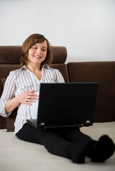 Pregnant woman working on laptop from home on sofa