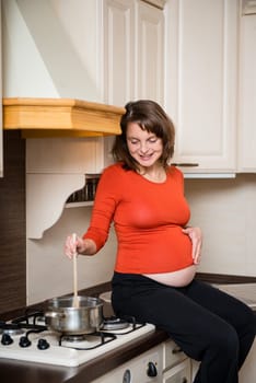 Lifestyle portrait of smiling pregnant woman cooking in home kitchen