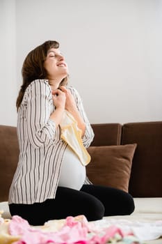 Pregnancy - woman enjoying and preparing baby clothes at home on sofa