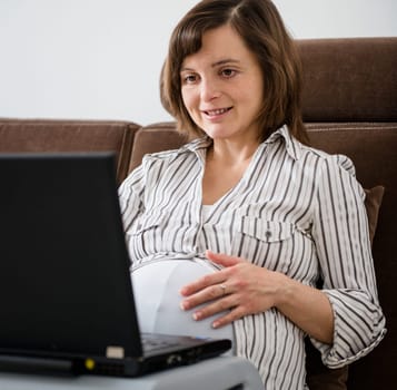 Pregnant woman working on laptop from home on sofa