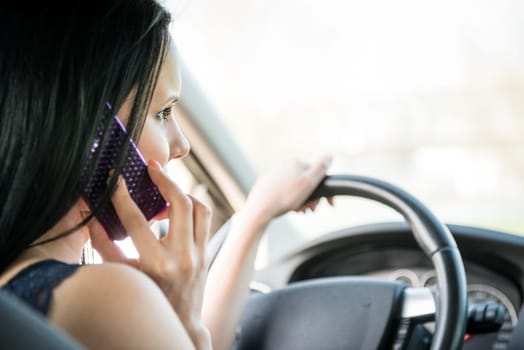 Young woman calling phone while driving car - rear view
