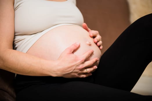 Detail of hands holding pregnant belly - indoors