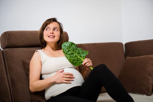 Lifestyle portrait of smiling pregnant woman eating spinach at home
