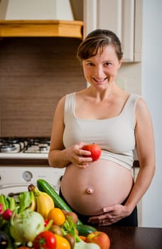 Pregnant woman with abundance of vegetables and fruits holding apple